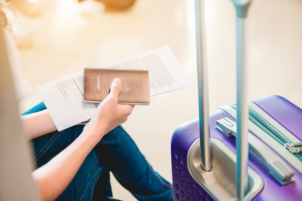 person holding passport and papers while sitting next to suitcase