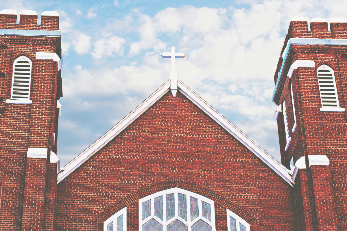 close up view of the top of a brick church with a cross on the peak of the roof