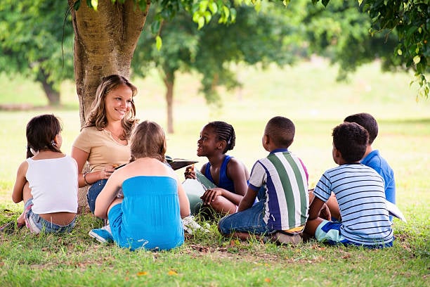 woman sitting under tree teaching a group of children